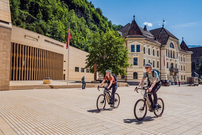 Velontour © Miriam Mayer Zwei Radfahrer vor historischen Gebäuden in sonnigem Stadtplatz
