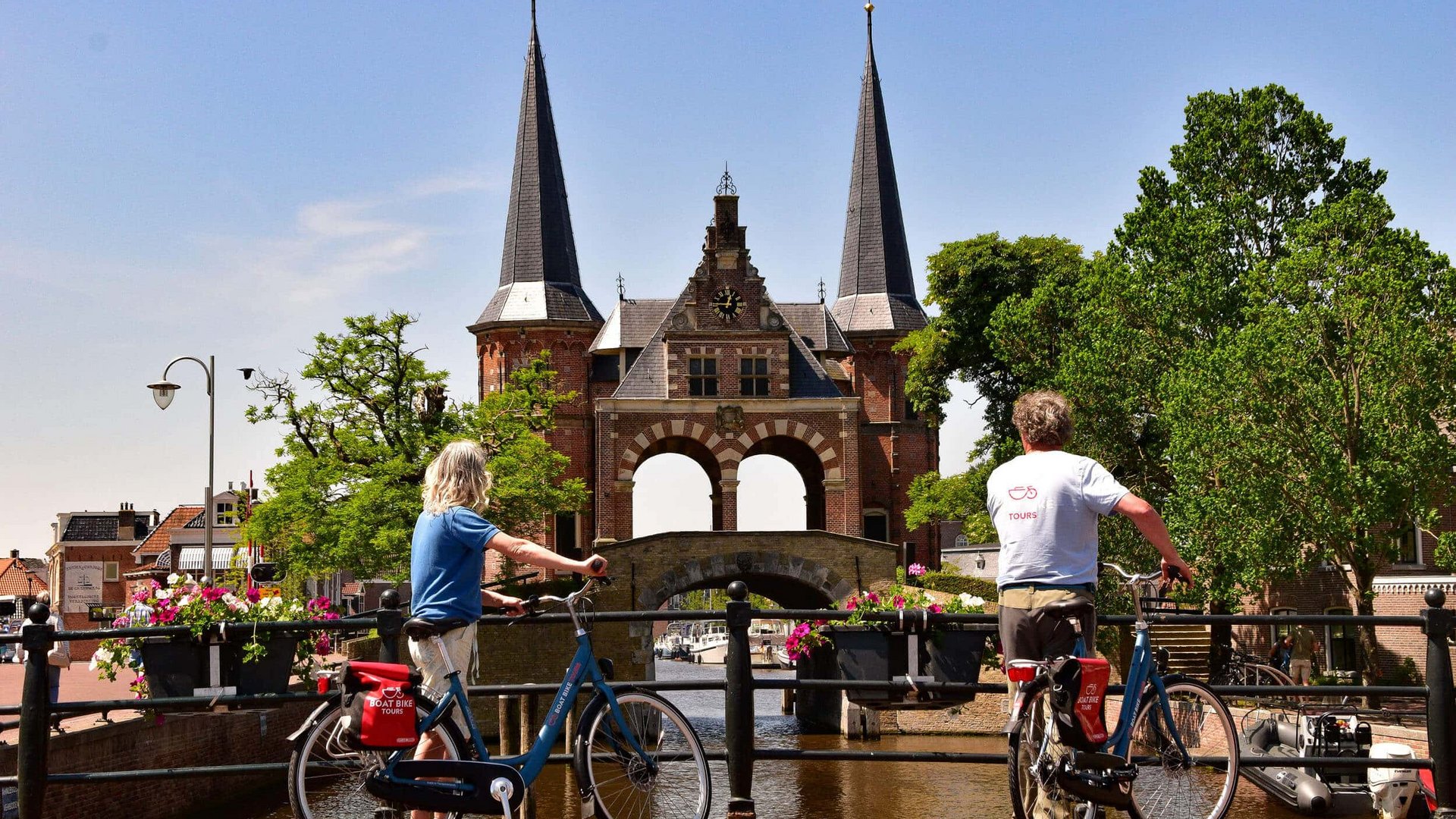 Rundreise Nordholland und Friesland © Boat Bike Tours Zwei Radfahrer betrachten ein historisches Tor an einem Kanal bei sonnigem Wetter