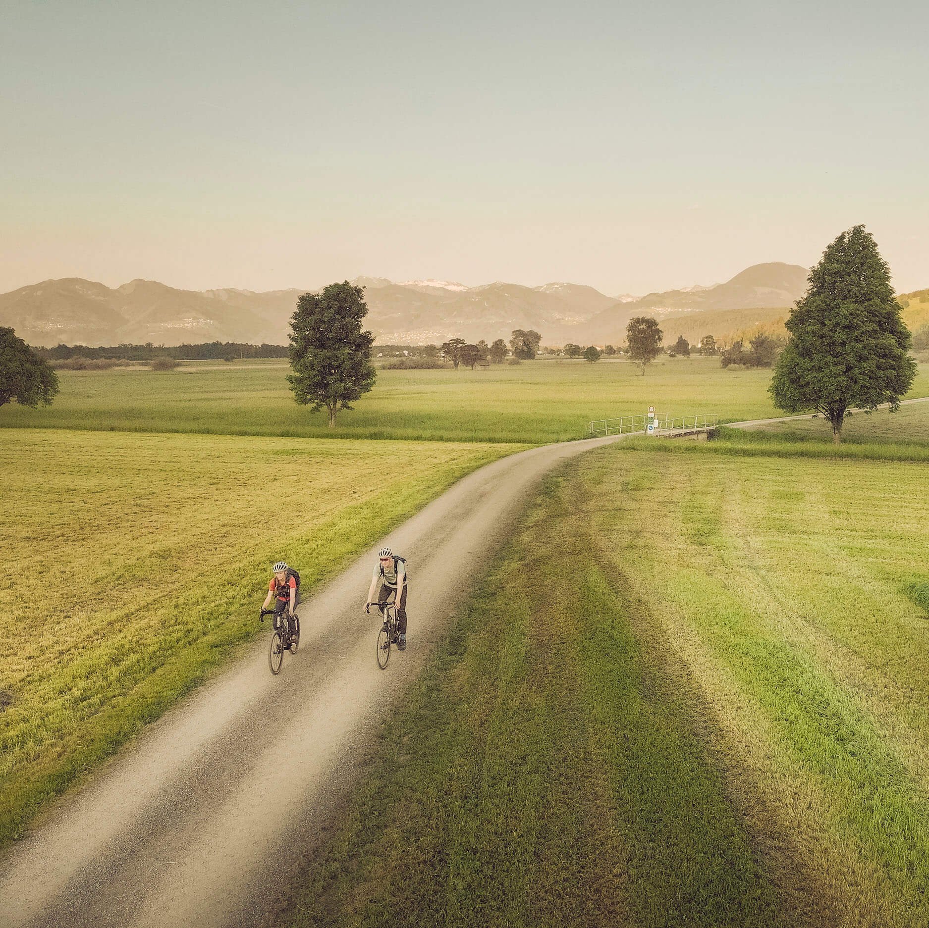 Liechtenstein: ein Land – ein Radweg © Miriam Mayer Zwei Radfahrer auf Landweg in grüner Landschaft mit Bergen im Hintergrund