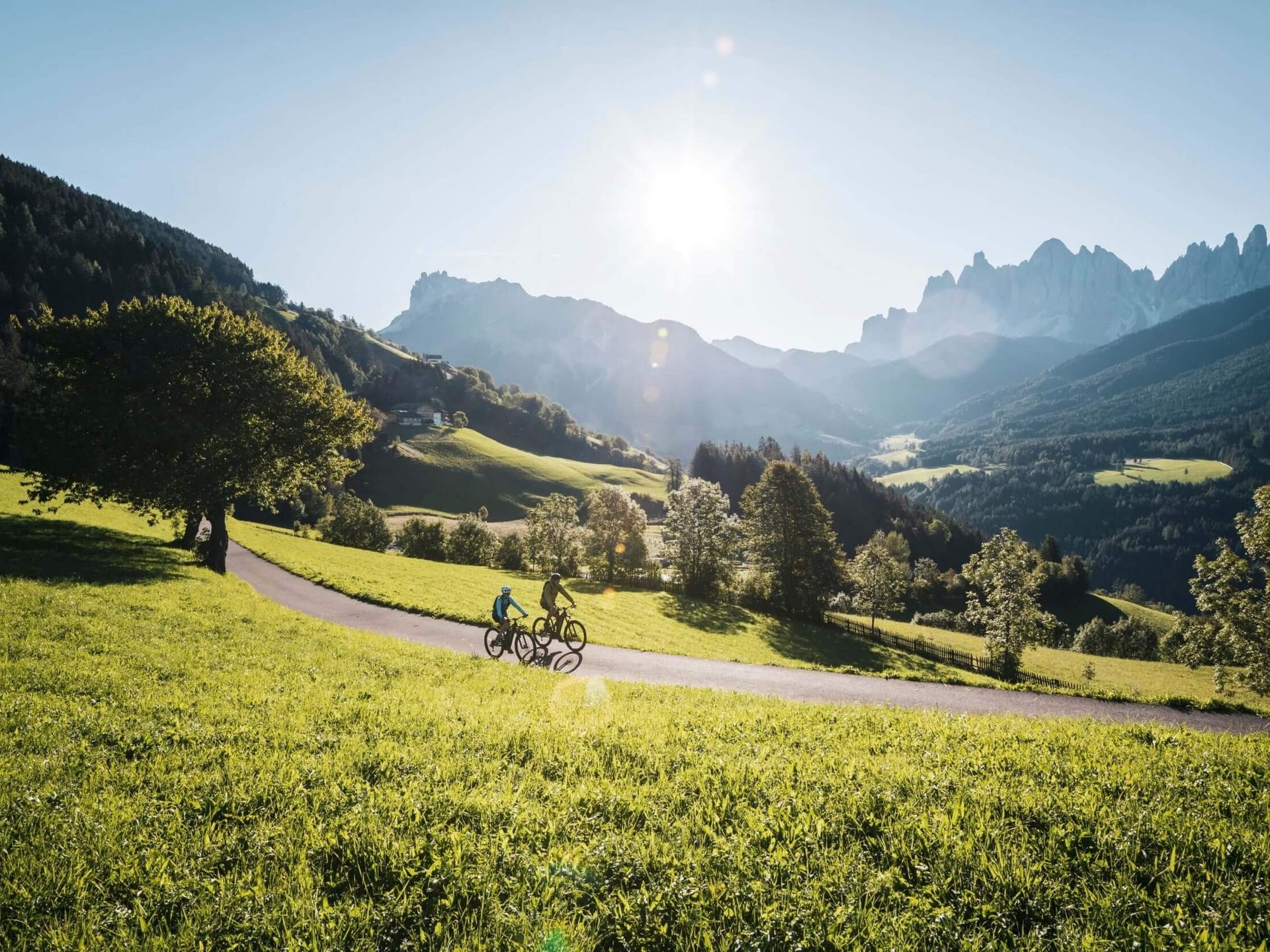 Zwei Radfahrer fahren auf einem Weg durch grüne Alpenlandschaft bei sonnigem Wetter
