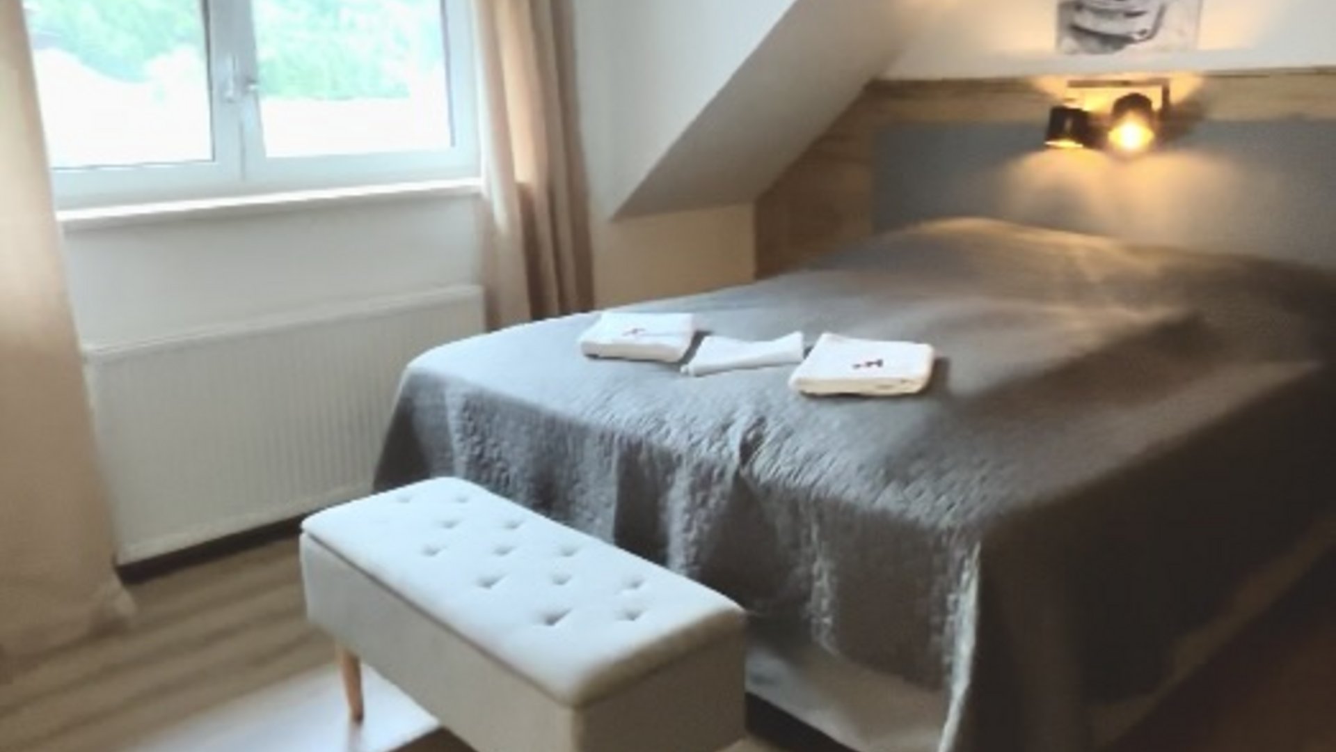 Schlafzimmer mit Doppelbett, grauer Bettdecke und Fenster mit Vorhängen