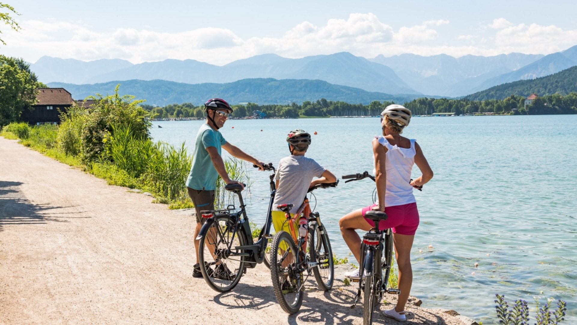 Tour-Detail Drei Radfahrer mit Helmen am See vor Bergen bei Sonnenschein