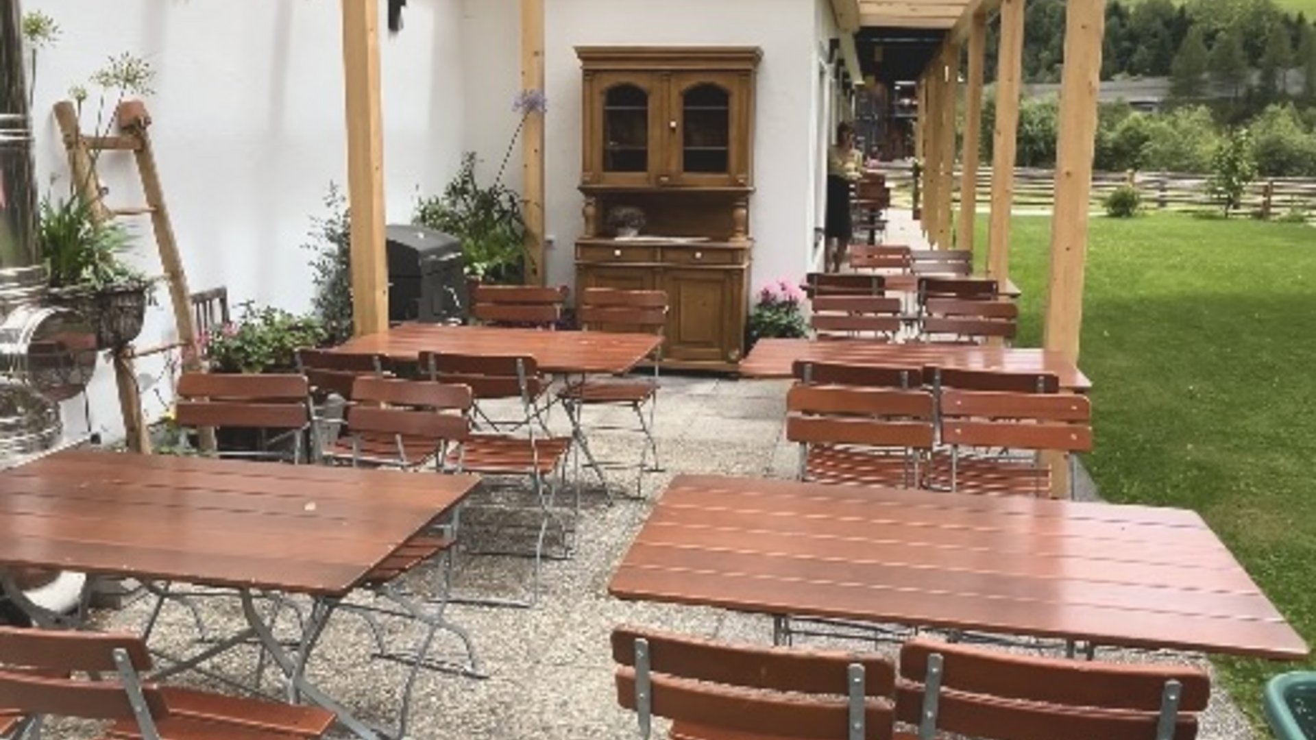 Überdachte Terrasse mit Holztischen und Bänken neben einer Wiese