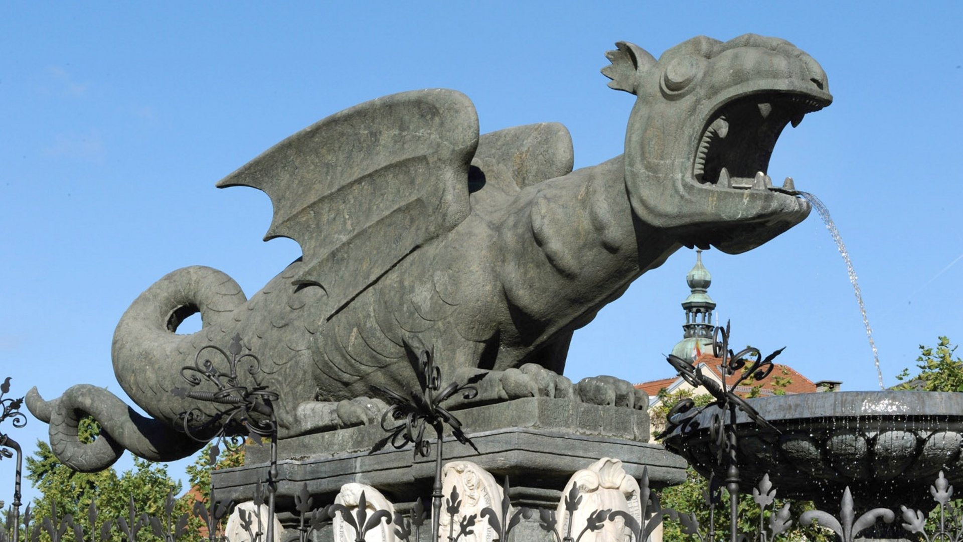 Tour-Detail Steinerner Drachenbrunnen mit Wasserfontäne vor blauem Himmel