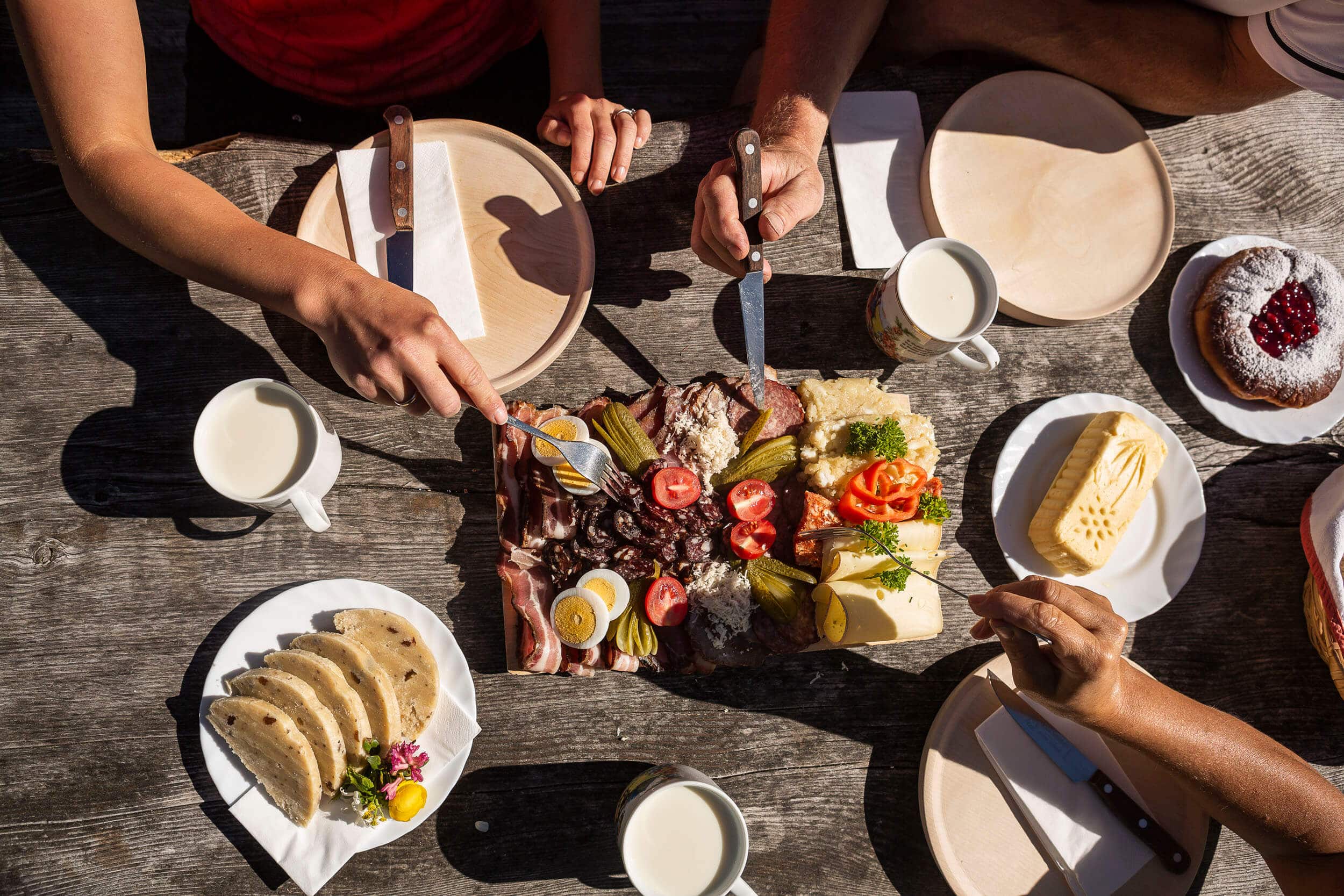 Menschen teilen eine Brotzeit mit Eiern, Käse, Wurst, Marmeladekuchen und Getränken