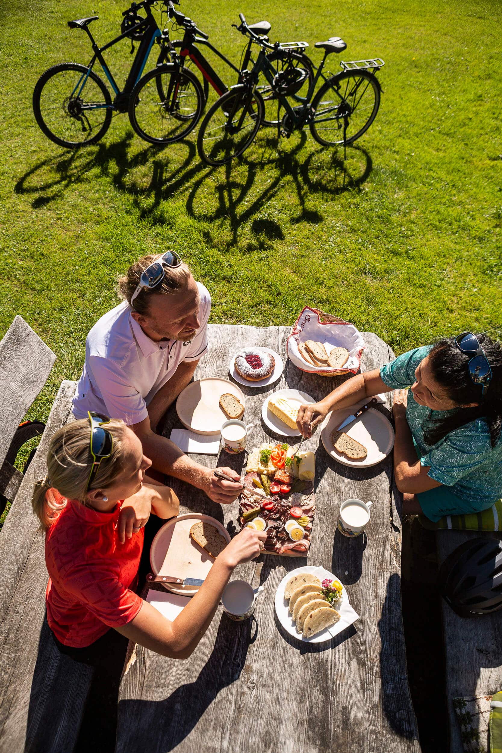 Drei Personen essen Picknick draußen neben Fahrrädern auf einer Wiese